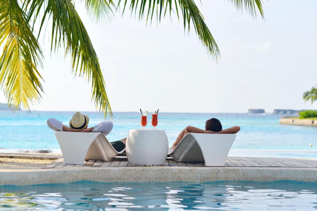 Pareja de viaje de novios en una isla paradisiaca toma unas bebidas sentados en la piscina privada mirando al mar
