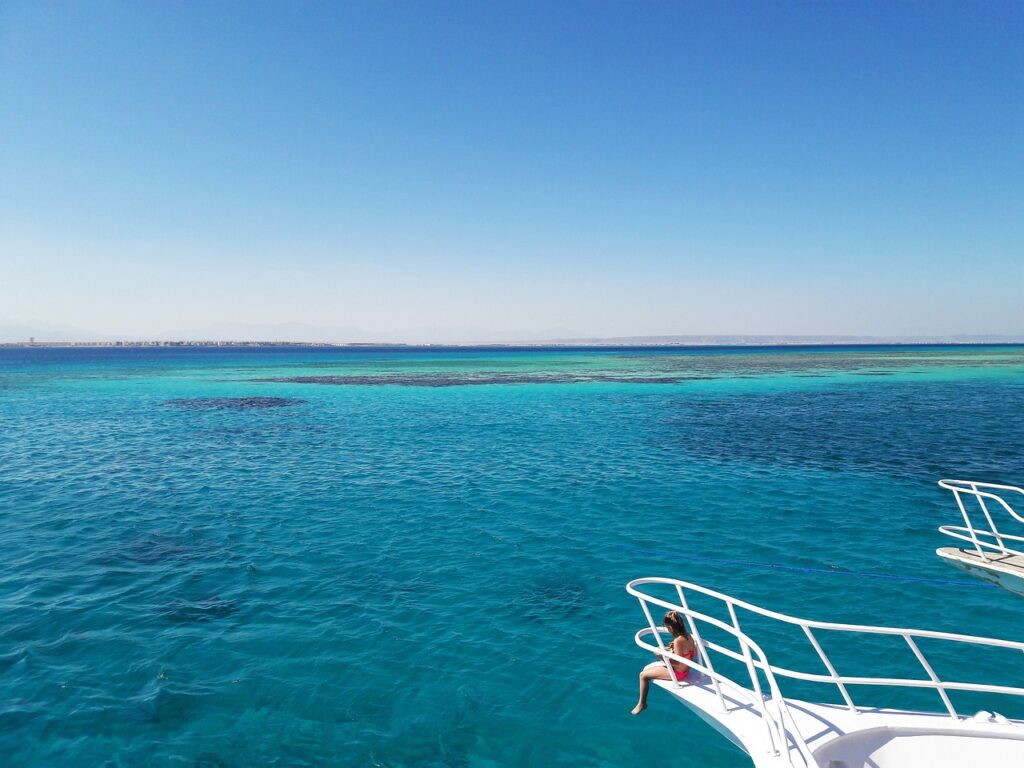 Niña sentada en el borde de un yate de recreo frente al azul intenso del Mar Rojo