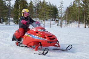 Niño en moto de nieve equipado con ropa de invierno en Laponia