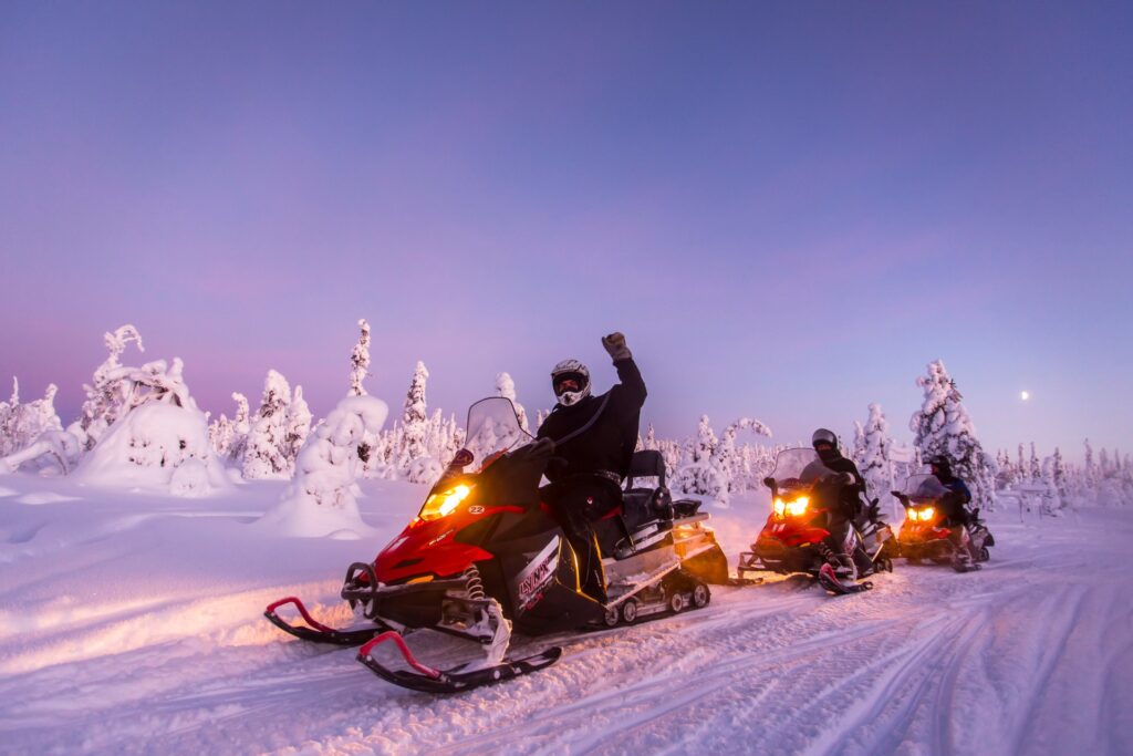 Grupo de turistas en safari de motonieves en Laponia pasan frente a bosque totalmente nevado y saludan a cámara