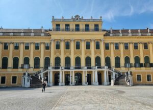 A view of the historic Schonbrunn Palace facade, featuring its grand architecture under a bright blue sky.