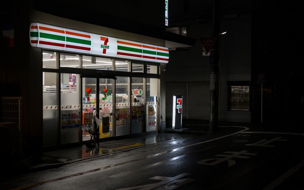 A 7-Eleven convenience store in rainy Kyoto at night, highlighting wet streets and urban atmosphere.